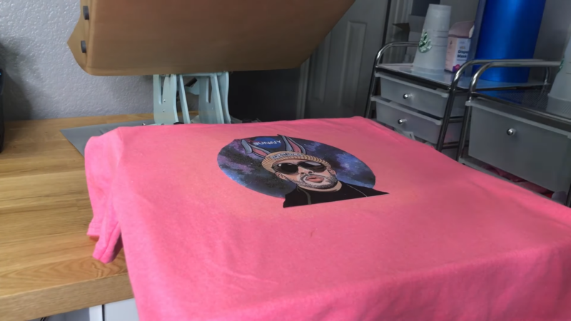 A Pink Shirt with A Printed Graphic Design Being Pressed with A Heat Transfer Vinyl (HTV) Machine