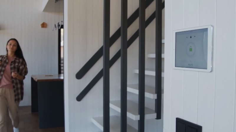 A Person Walking Past a Wall-Mounted Security Panel in A Modern Home with A Staircase in The Background