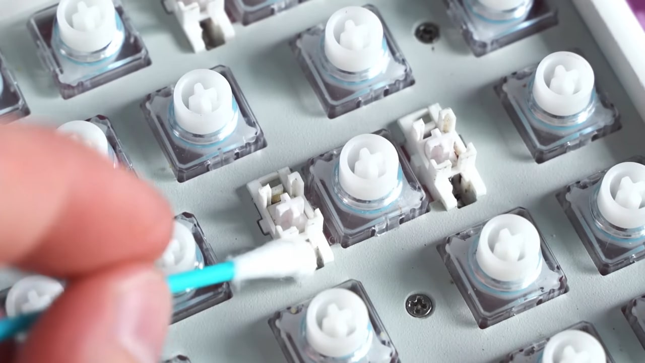 Close-up of a person using a cotton swab to clean mechanical keyboard switches and stabilizers.