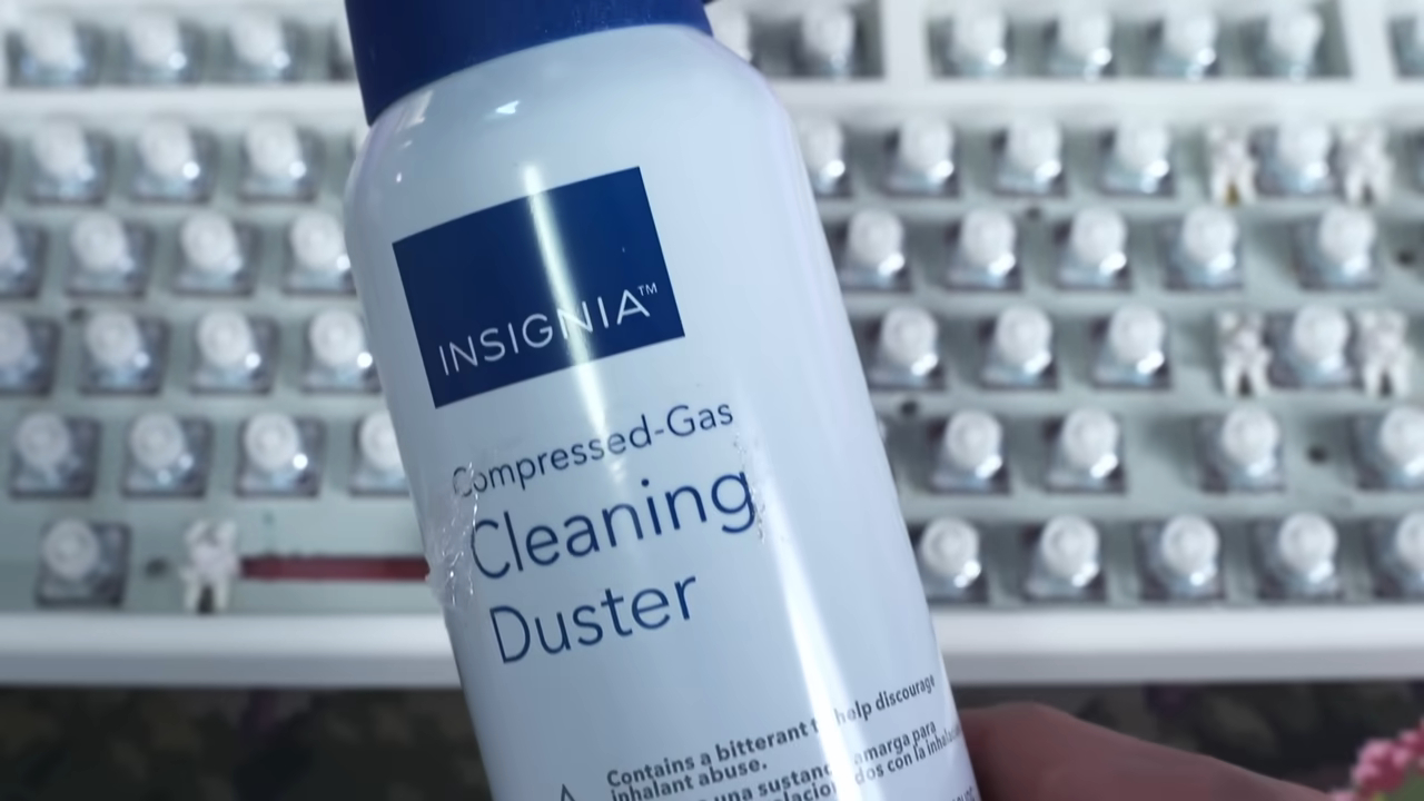 Close-up of an Insignia compressed-gas cleaning duster held in front of a mechanical keyboard with removed keycaps