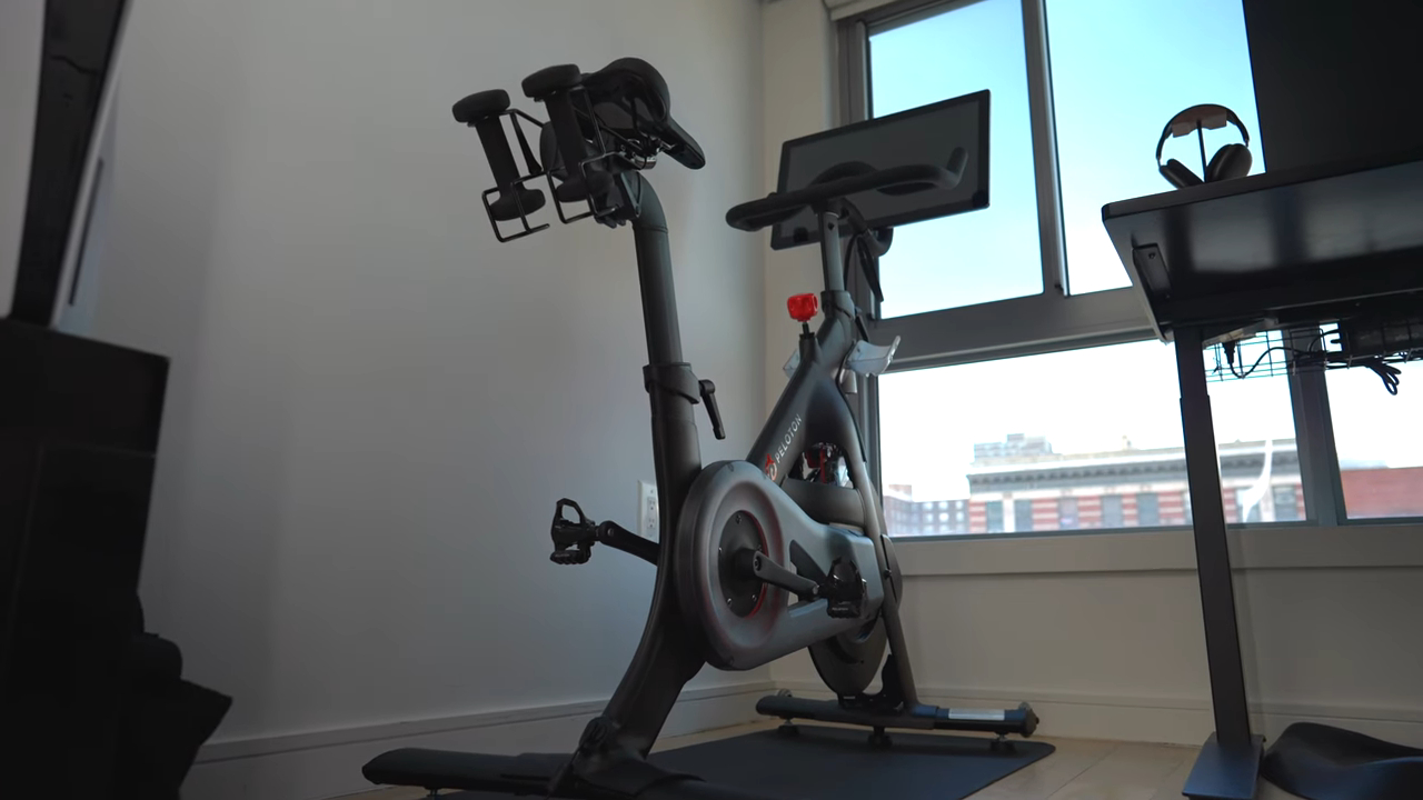 Peloton exercise bike set up in a modern home gym space near a large window with natural light and a city view
