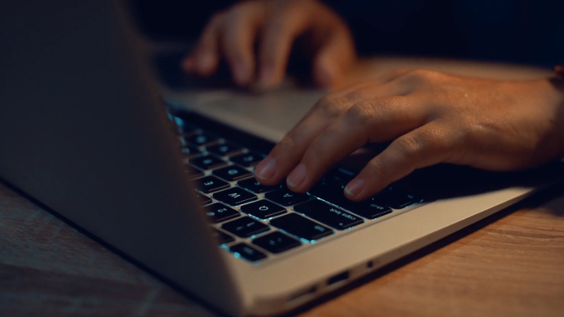 Close-up of hands typing on a laptop keyboard in low light