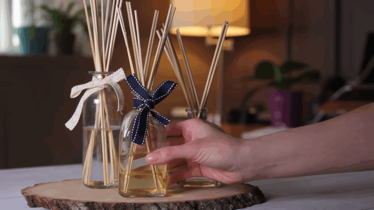 A hand adjusting a stylish aroma diffuser with reed sticks and a decorative ribbon