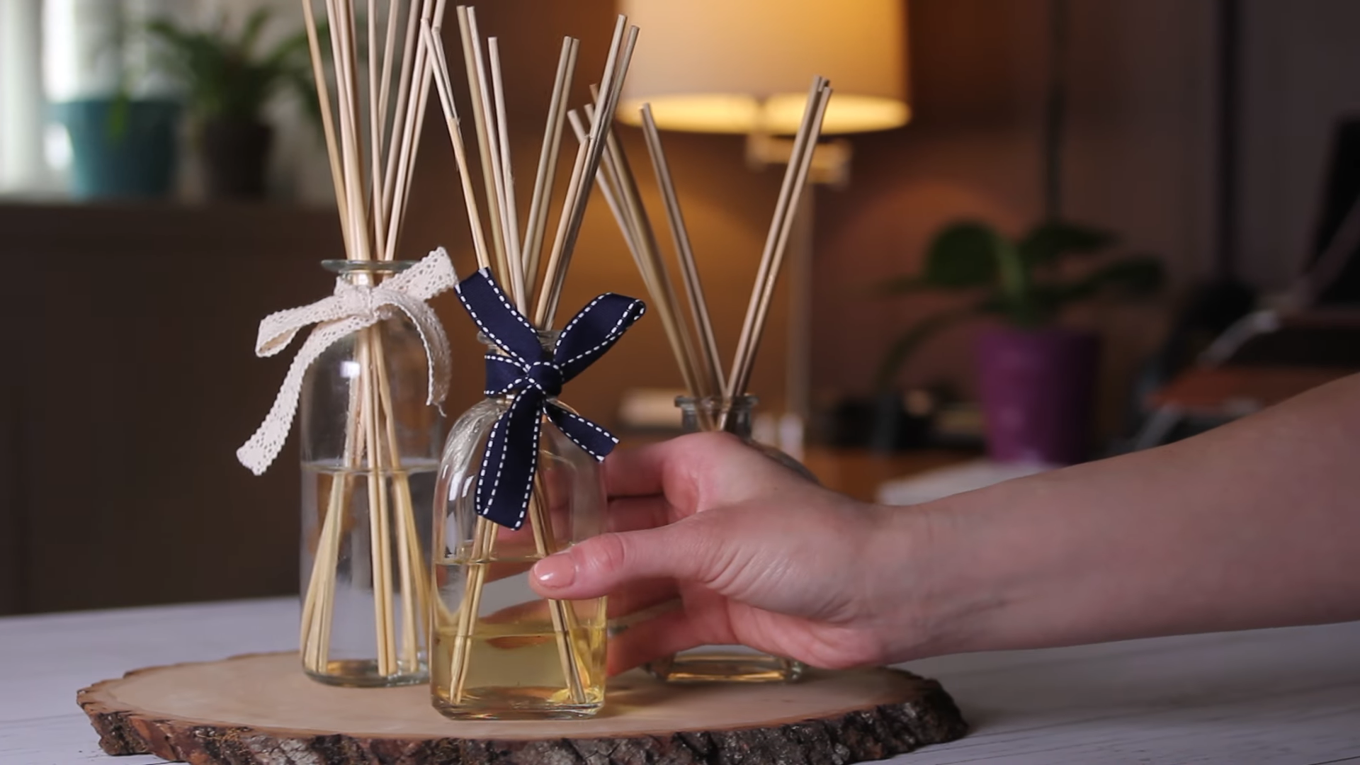 A hand adjusting a stylish aroma diffuser with reed sticks and a decorative ribbon
