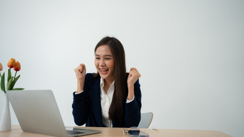 A woman celebrates a milestone while working on her laptop, representing success in building an online business in Asia