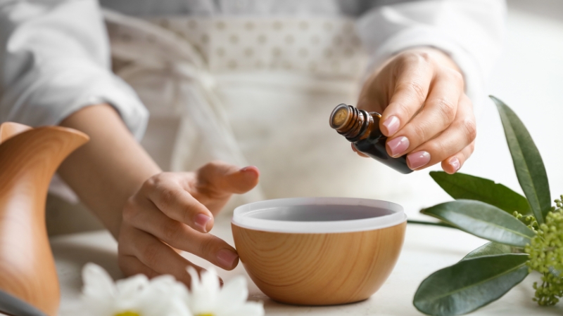A person adding essential oil to a wooden aroma diffuser bowl
