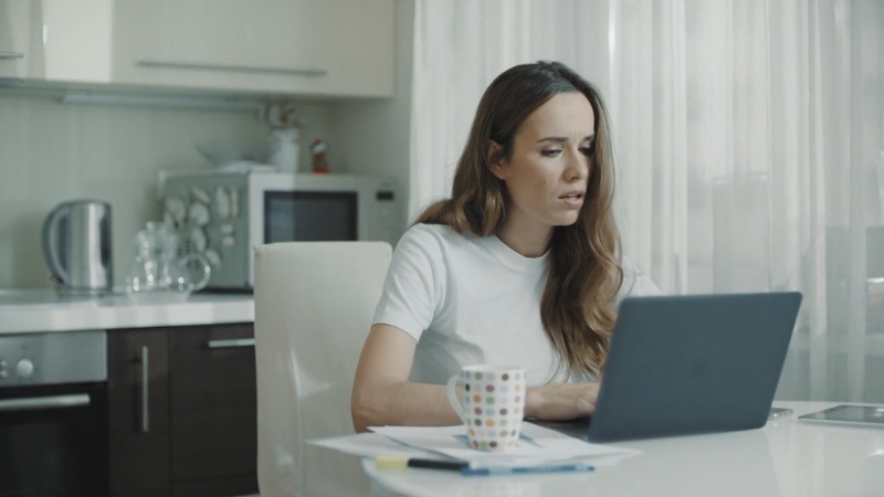 Woman sitting at a kitchen table looking frustrated with a laptop frozen in front of her